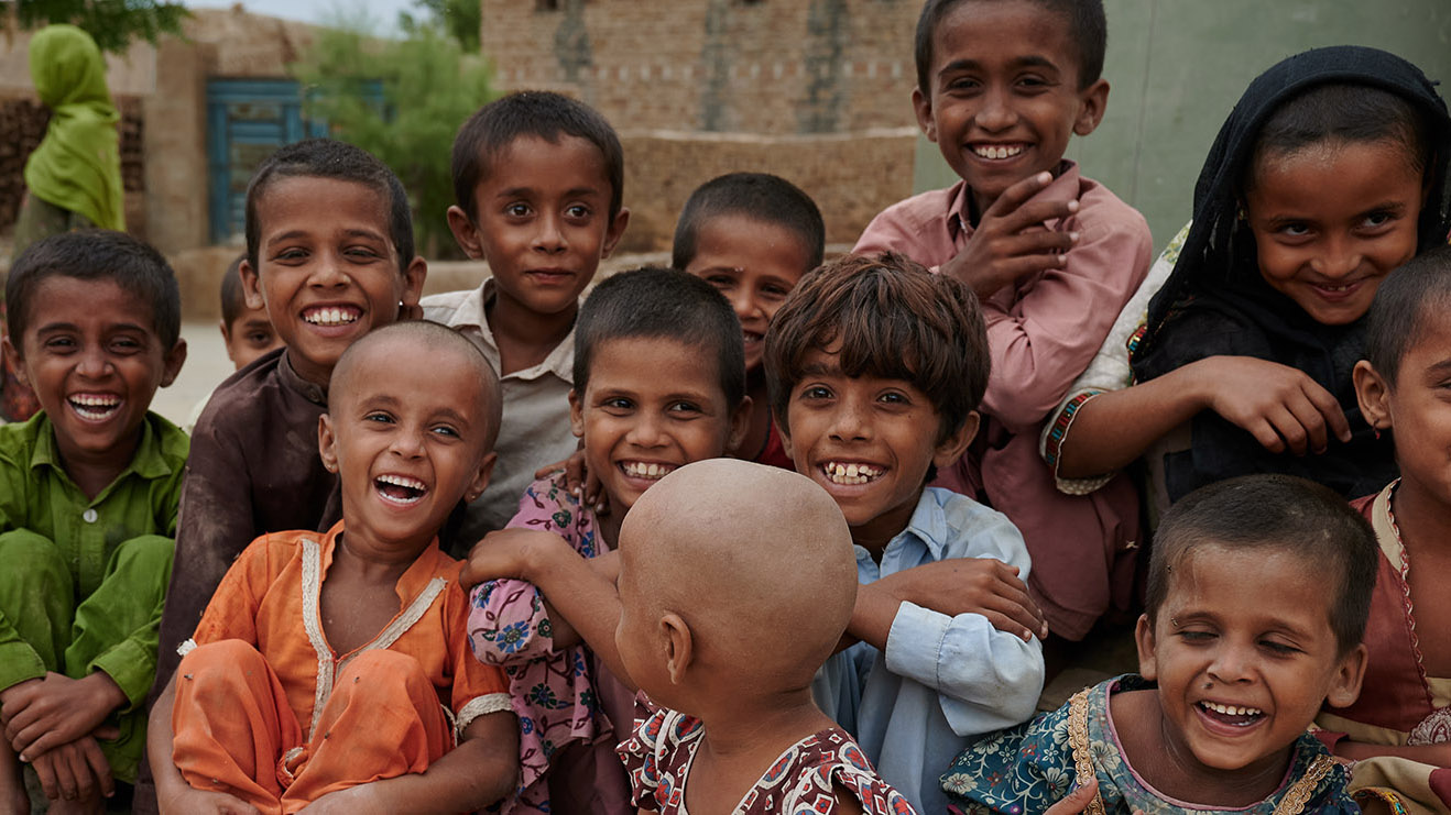 On 12 September 2022, posing for a picture, a group of children smile in village Ismail Bhand, Shaheed Benazirabad district, Sindh province, Pakistan.In Pakistan, village Ismail Bhand has been severely affected by the flood. All the road communications has been cut off and it has turned into an island now. There is only one country boat that ferries people back and forth. The village residents has not receive much assistance from anyone. UNICEF support mobile team is one of the first to reach the location and provide medical assistance to the villagers. Like most flooded affected areas, this village too is swamped with malaria and water-borne diseases. Hundreds of homes has been damaged, some completely gone. People here are in desperate need for assistance.UNICEF has provided six flood affected districts with three mobile health units each. These mobile units visit different flood affected locations every day to provide women and children with immediately needed medical attention, nutrition support, immunization, and other health services, including malaria testing and medication. These units include community health workers from district-based partner organizations, doctors, nursing staff and a consignment of various medicine and vaccines.